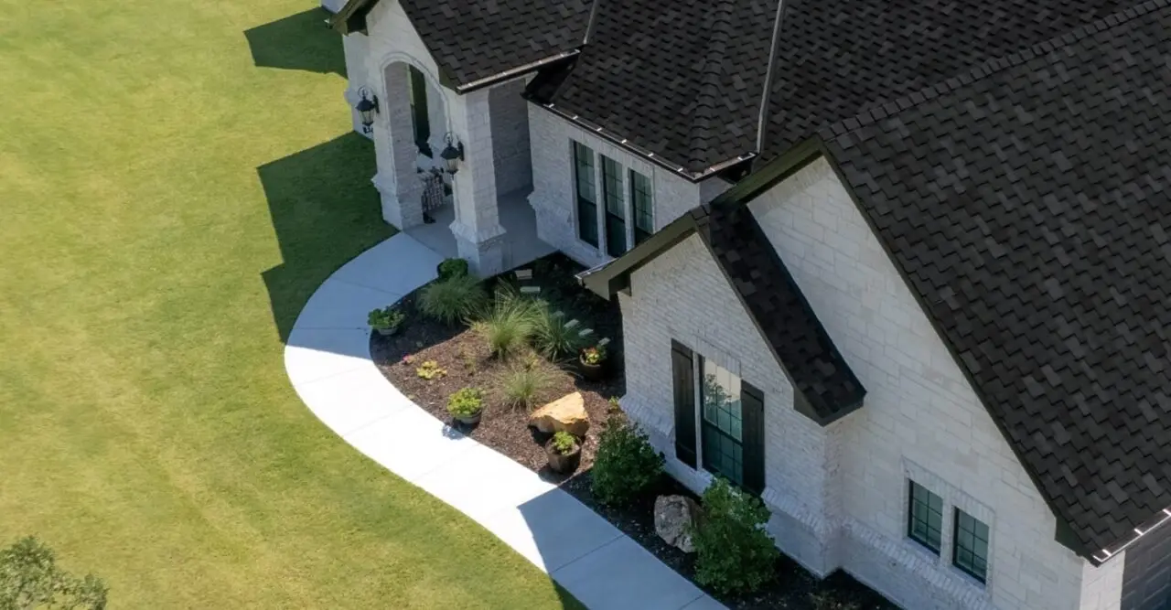 Aerial view of a completed architectural-shingle roof replacement on a white stone home